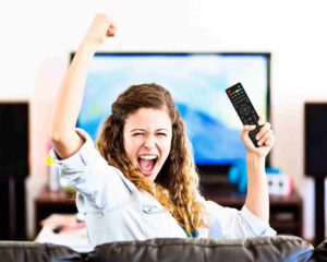 Enthusiastic young female spectator turns from TV cheering triumphantly